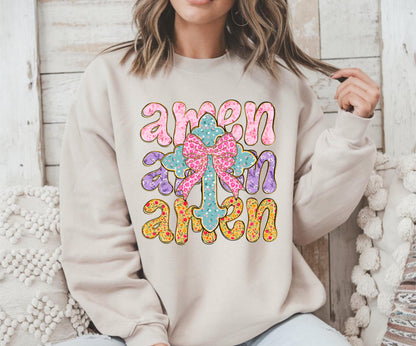 May include: A beige sweatshirt with a floral cross design and the word "amen" repeated three times in a colorful, stylized font.