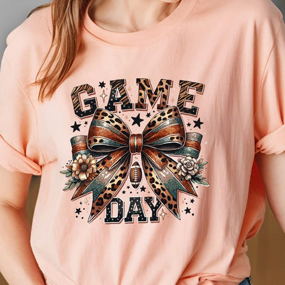 May include: A pink t-shirt with a graphic of a leopard print bow with glitter and the words "GAME DAY" in black.