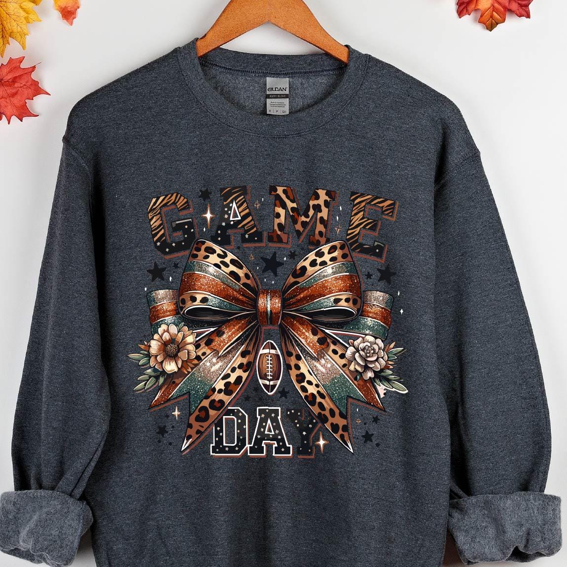 May include: A dark gray sweatshirt with a graphic print of a leopard print bow with the words "GAME DAY" in brown and gold lettering.