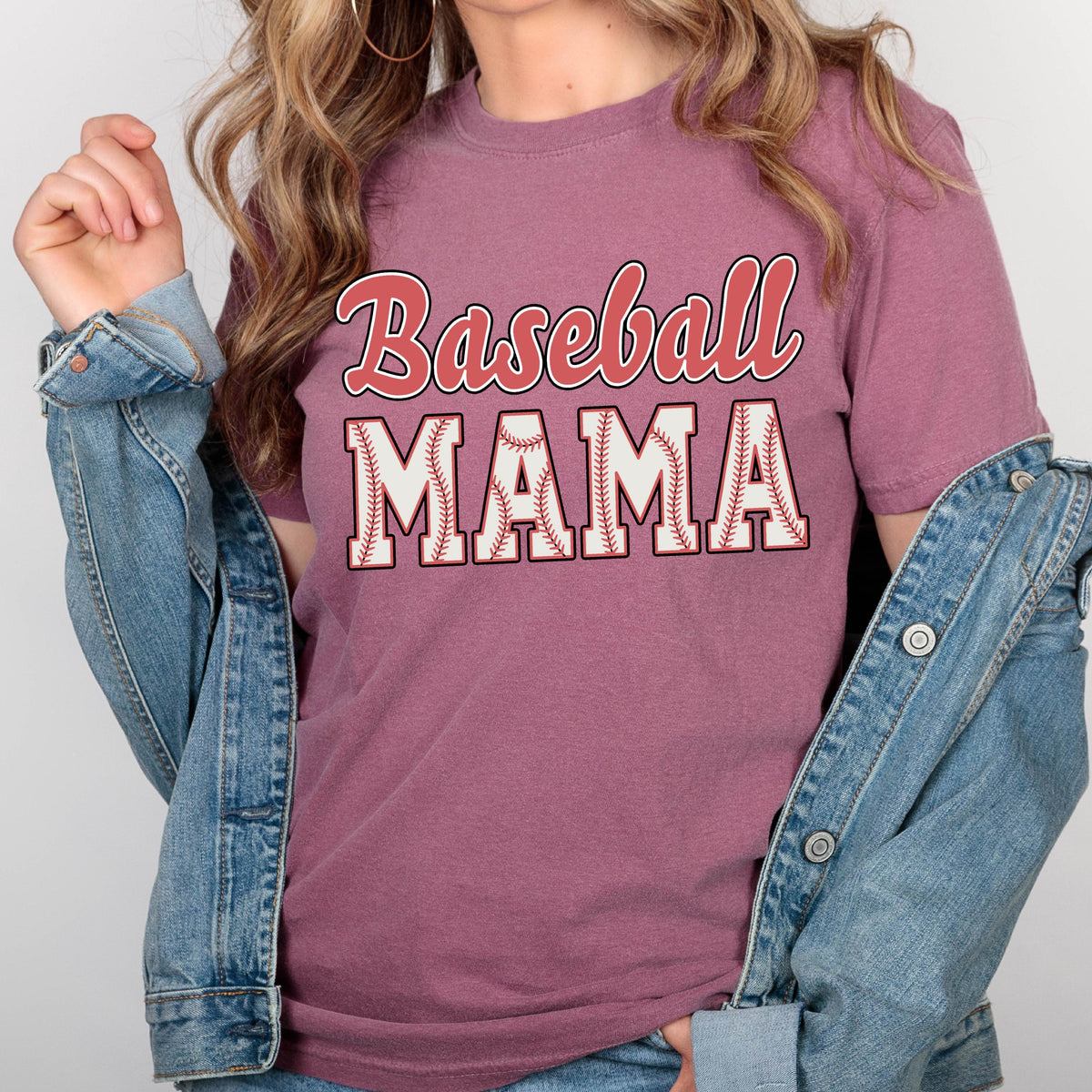 May include: A mauve t-shirt with the text "Baseball Mama" in red and white lettering. The letters are outlined in white and have a baseball stitch pattern.