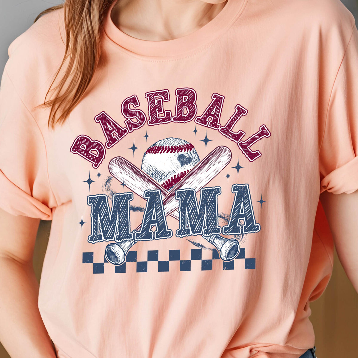 May include: A peach-colored t-shirt with a baseball-themed graphic. The graphic features two crossed baseball bats, a baseball, and the text "Baseball Mama".