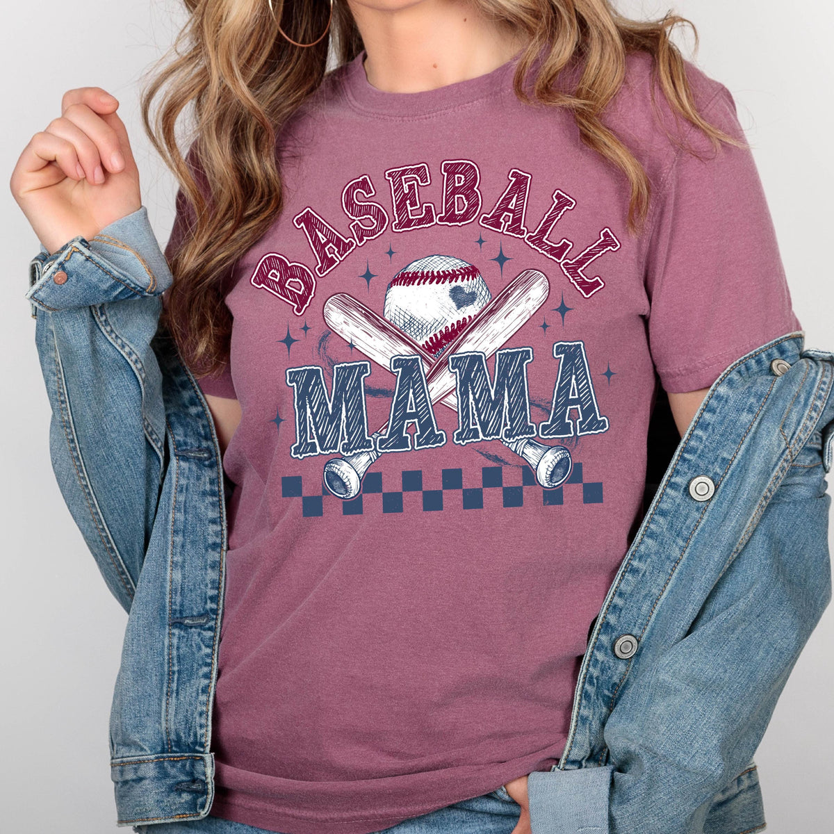 May include: A mauve t-shirt with a baseball graphic and the text "BASEBALL MAMA" in a white and blue font. The graphic features a baseball, two crossed bats, and a checkered pattern.
