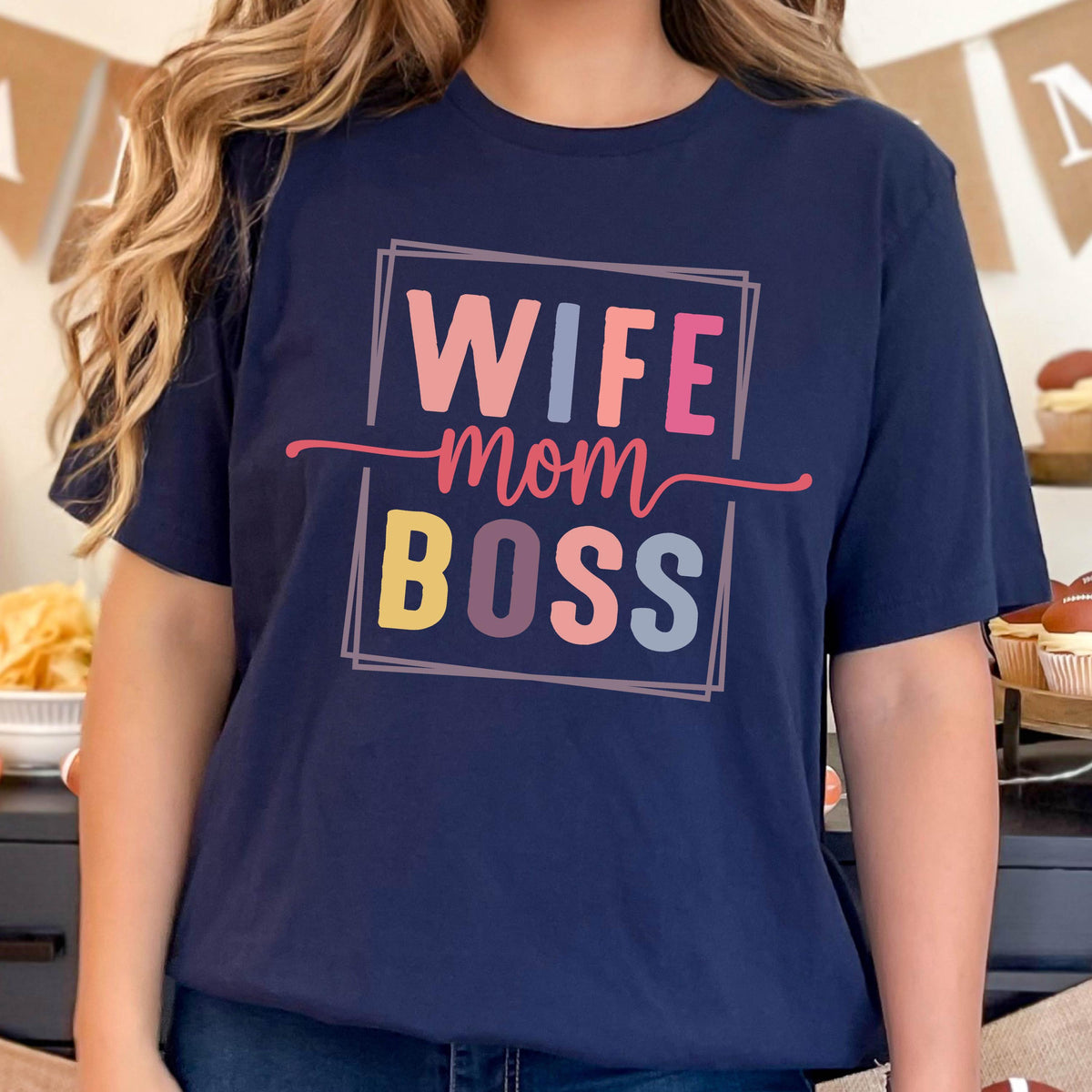 May include: Navy blue t-shirt with the words "WIFE mom BOSS" in a colorful, framed design. The text is in pink, blue, yellow, and purple. The shirt is a casual style.