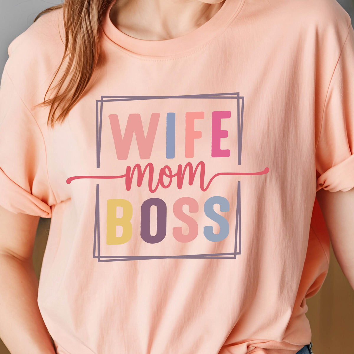 May include: A peach-colored t-shirt with the words "WIFE mom BOSS" in a colorful, rectangular design. The text is in a mix of pink, blue, yellow, and purple. The shirt has short sleeves.