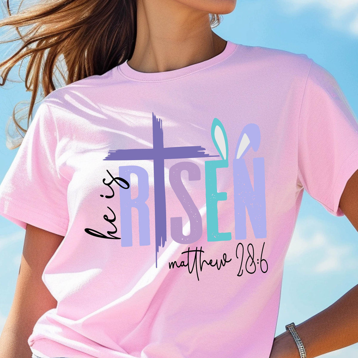 May include: Pink t-shirt with a purple and teal graphic that says "He is Risen" with a cross and bunny ears. The text "Matthew 28:6" is below the graphic.