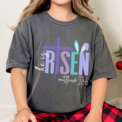 May include: A gray t-shirt with a colorful graphic that says "He is Risen" with a cross and bunny ears. The text "Matthew 28:6" is below the graphic.
