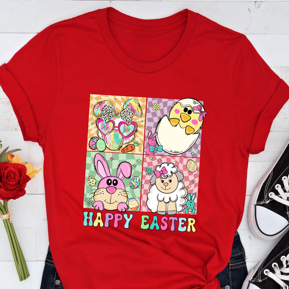 May include: A red t-shirt featuring a colorful graphic with Easter-themed characters. The design includes a bunny wearing sunglasses, a chick hatching from an egg, a pink bunny, and a sheep. The words "HAPPY EASTER" are written below the images.