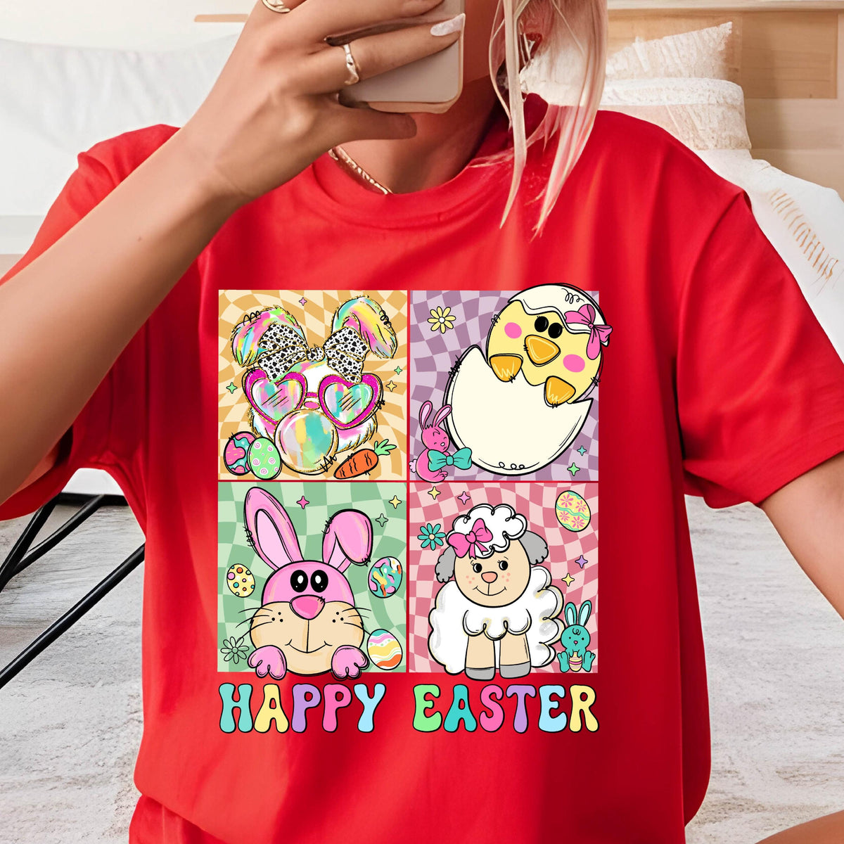 May include: Red t-shirt with a graphic of four cartoon animals: a bunny wearing sunglasses, a chick hatching from an egg, a bunny holding an egg, and a lamb. The graphic is surrounded by a checkered pattern and the text "HAPPY EASTER" is printed below.