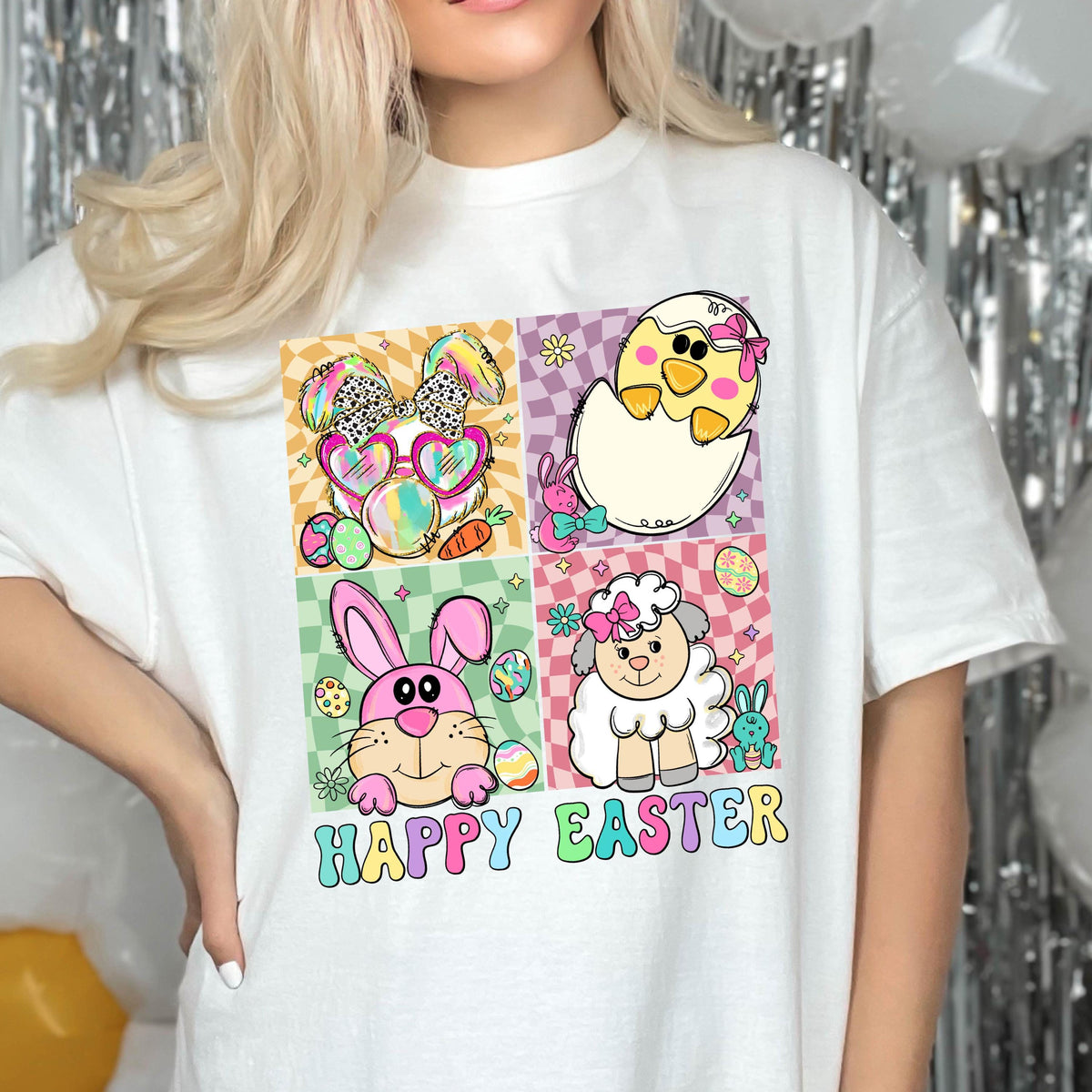 May include: White t-shirt with a colorful graphic design featuring a bunny, chick, lamb, and eggs. The text "Happy Easter" is printed below the graphic.
