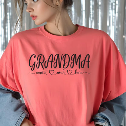 May include: A pink t-shirt with the text "Grandma" in black cursive lettering. Below the text are the names "Amelia", "Noah", and "Luna" with a heart symbol between each name.
