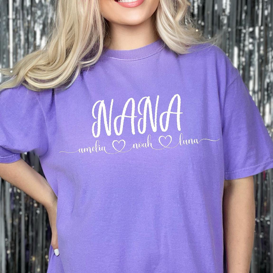 May include: Purple t-shirt with the word "NANA" in white script and the names "amelia", "noah", and "luna" written below with hearts between each name.