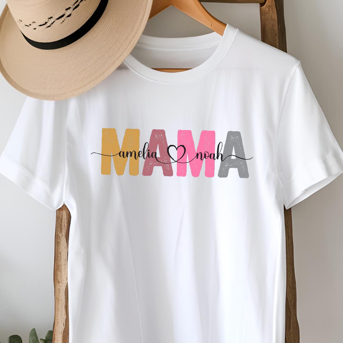 May include: White t-shirt with the word "MAMA" in colorful, textured letters. The names "amelia" and "noah" are written in cursive script below the word "MAMA" with a heart symbol between the names.