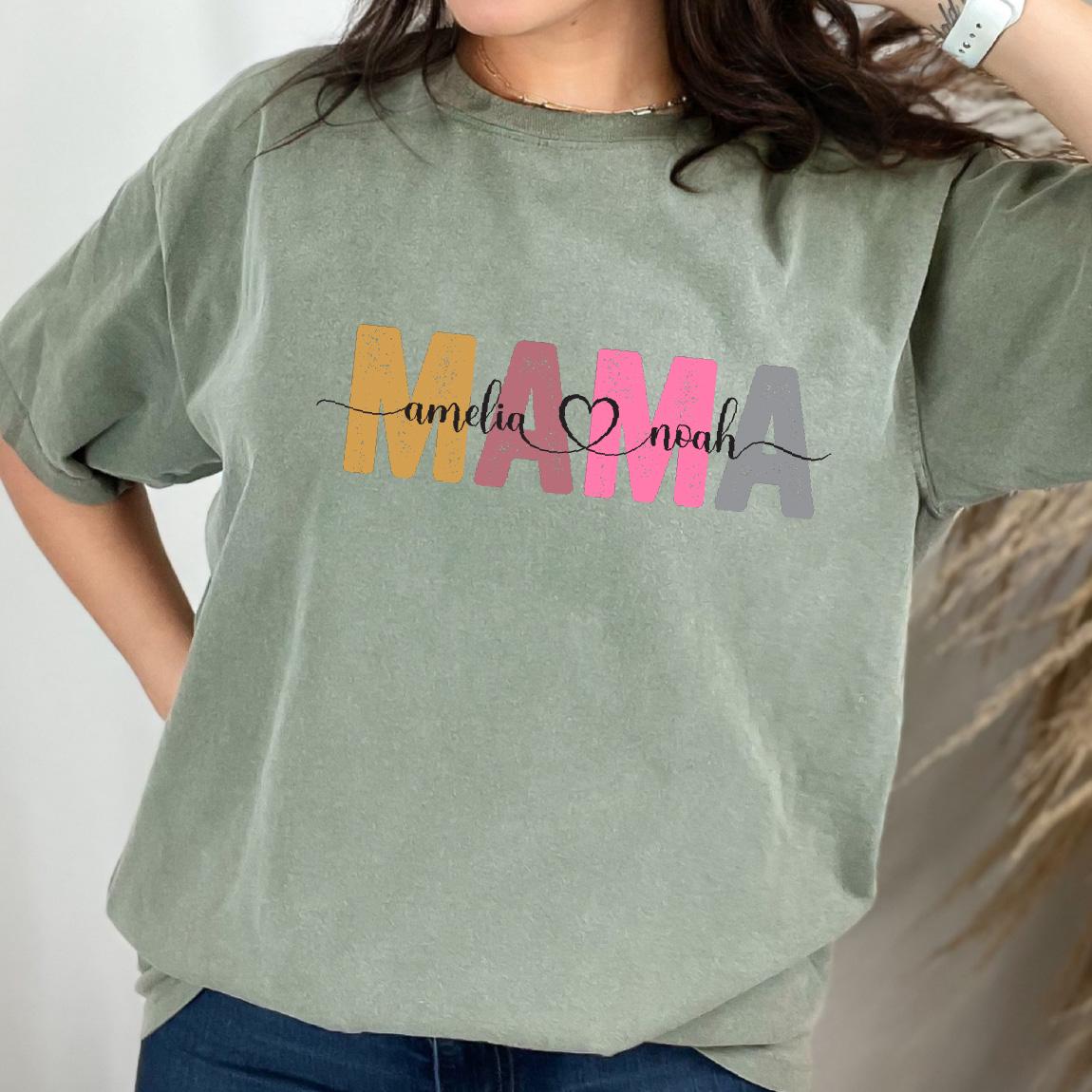 May include: A green t-shirt with the word "MAMA" in colorful letters. The letters are outlined in black and the word "amelia" is written in black script to the left of the "M" and the word "noah" is written in black script to the right of the "A".