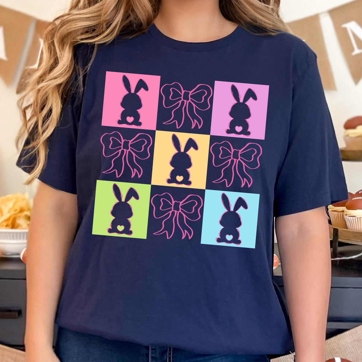 May include: A navy blue t-shirt with a colorful graphic design featuring silhouettes of bunnies and bows. The design is in a grid pattern with each square having a different color.