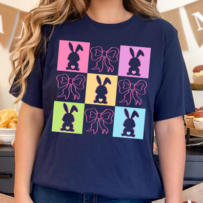 May include: A navy blue t-shirt with a colorful graphic design featuring silhouettes of bunnies and bows. The design is in a grid pattern with each square having a different color.