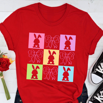 May include: Red t-shirt with a colorful design of bunnies and bows. The design is made up of nine squares, each with a different color and a bunny with a heart in the center. The bunnies are all facing forward and have long ears.