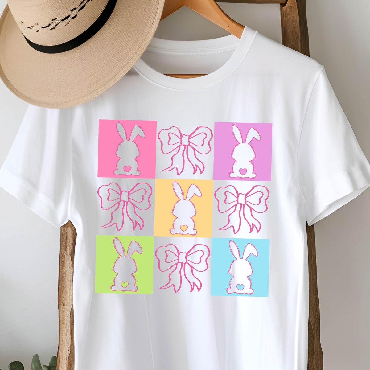 May include: White t-shirt with a colorful design of nine bunny silhouettes with bows. Each bunny is in a different colored square.