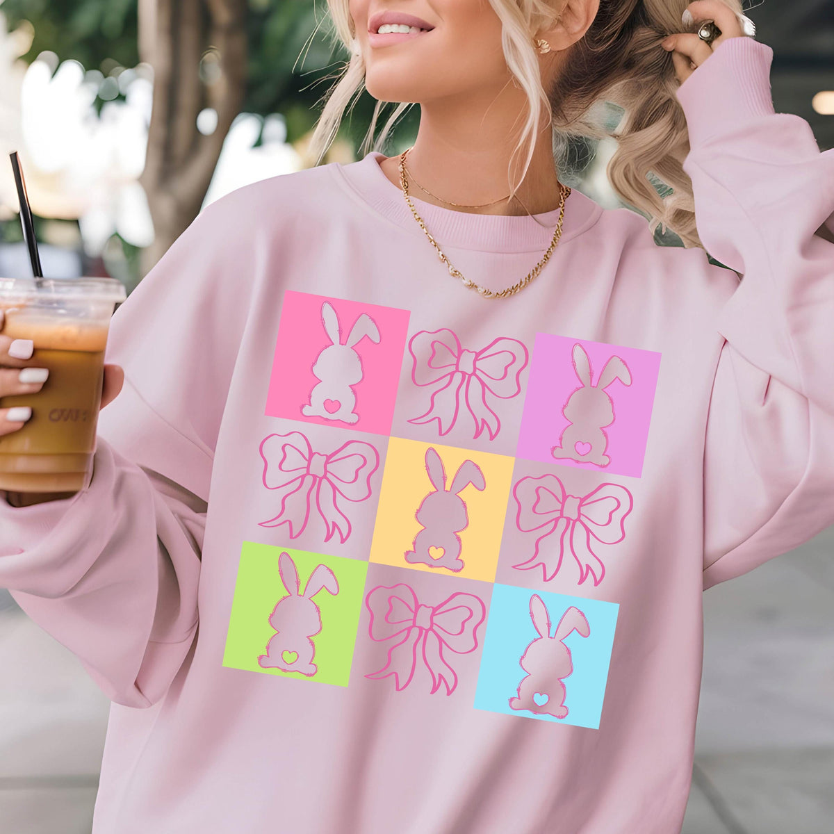 May include: Pink sweatshirt with a graphic design of bunnies and bows in a grid pattern. The squares are in different colors, including pink, yellow, blue, green, and light blue.
