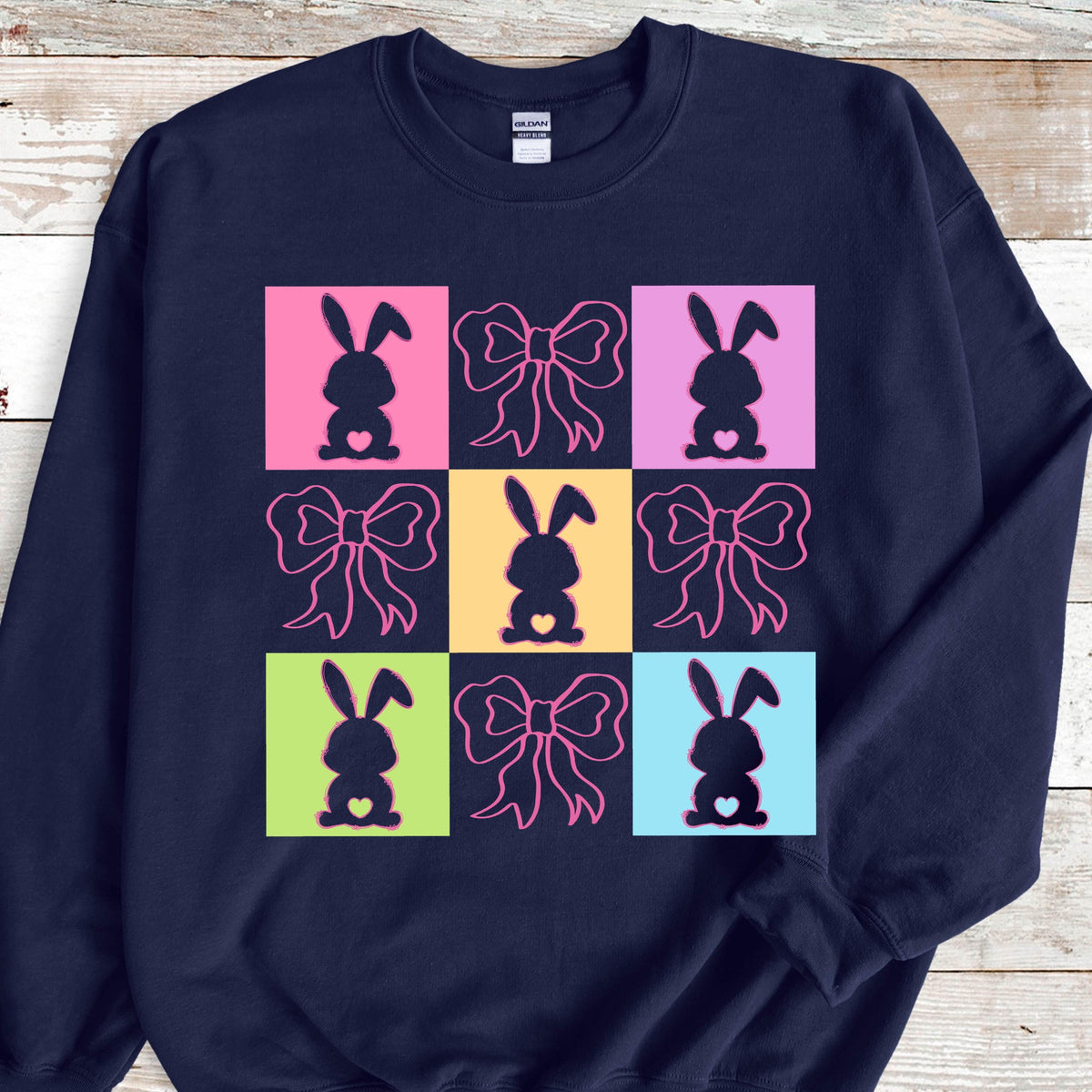 May include: Navy blue sweatshirt with a colorful design of nine squares featuring pink bows and bunny silhouettes.