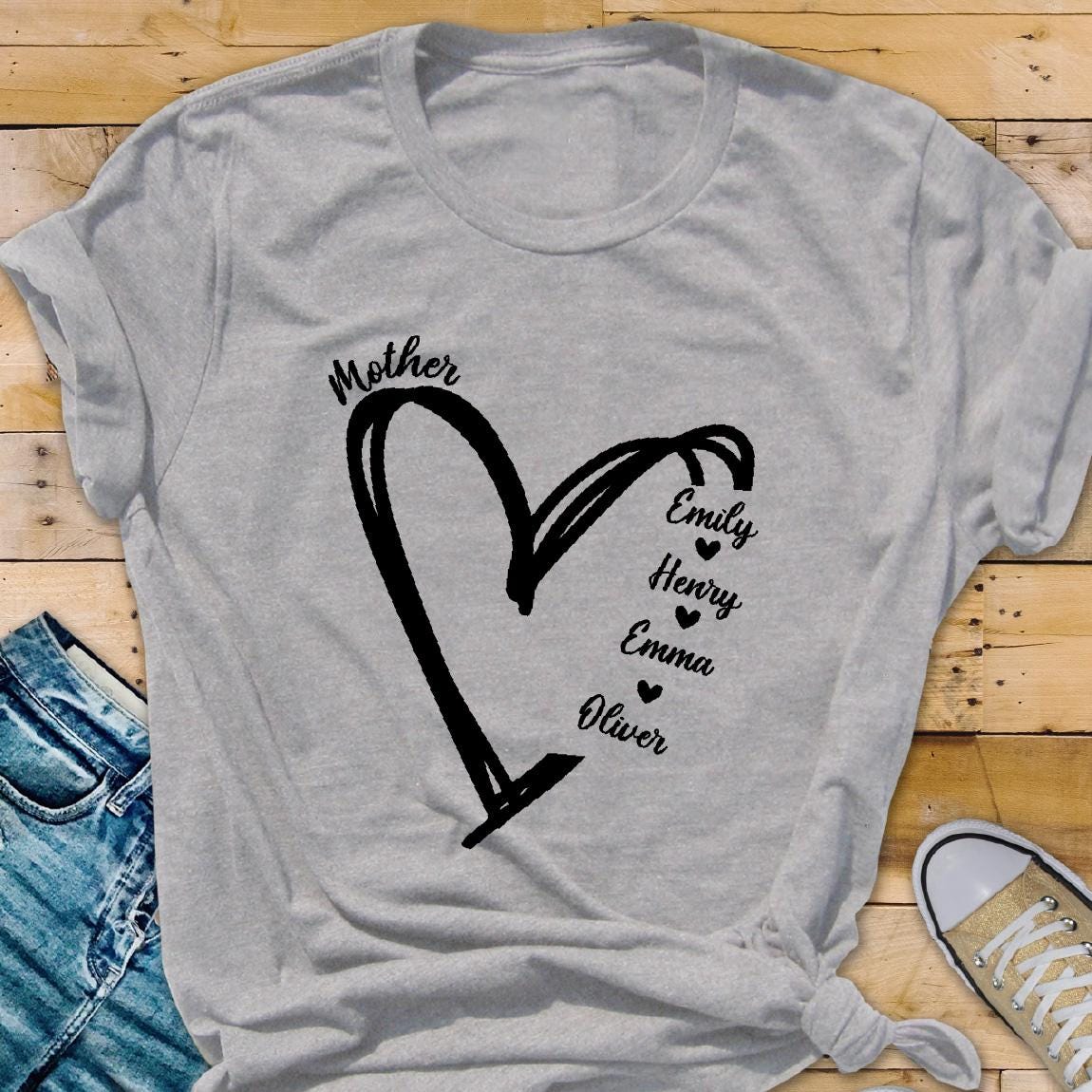 May include: Gray t-shirt with a black heart design and the word "Mother" above it. Inside the heart are the names "Emily", "Henry", "Emma", and "Oliver" with a small heart next to each name.