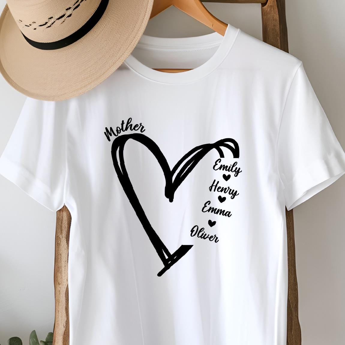 May include: White t-shirt with a black heart design and the word "Mother" above it. Inside the heart are the names Emily, Henry, Emma, and Oliver.