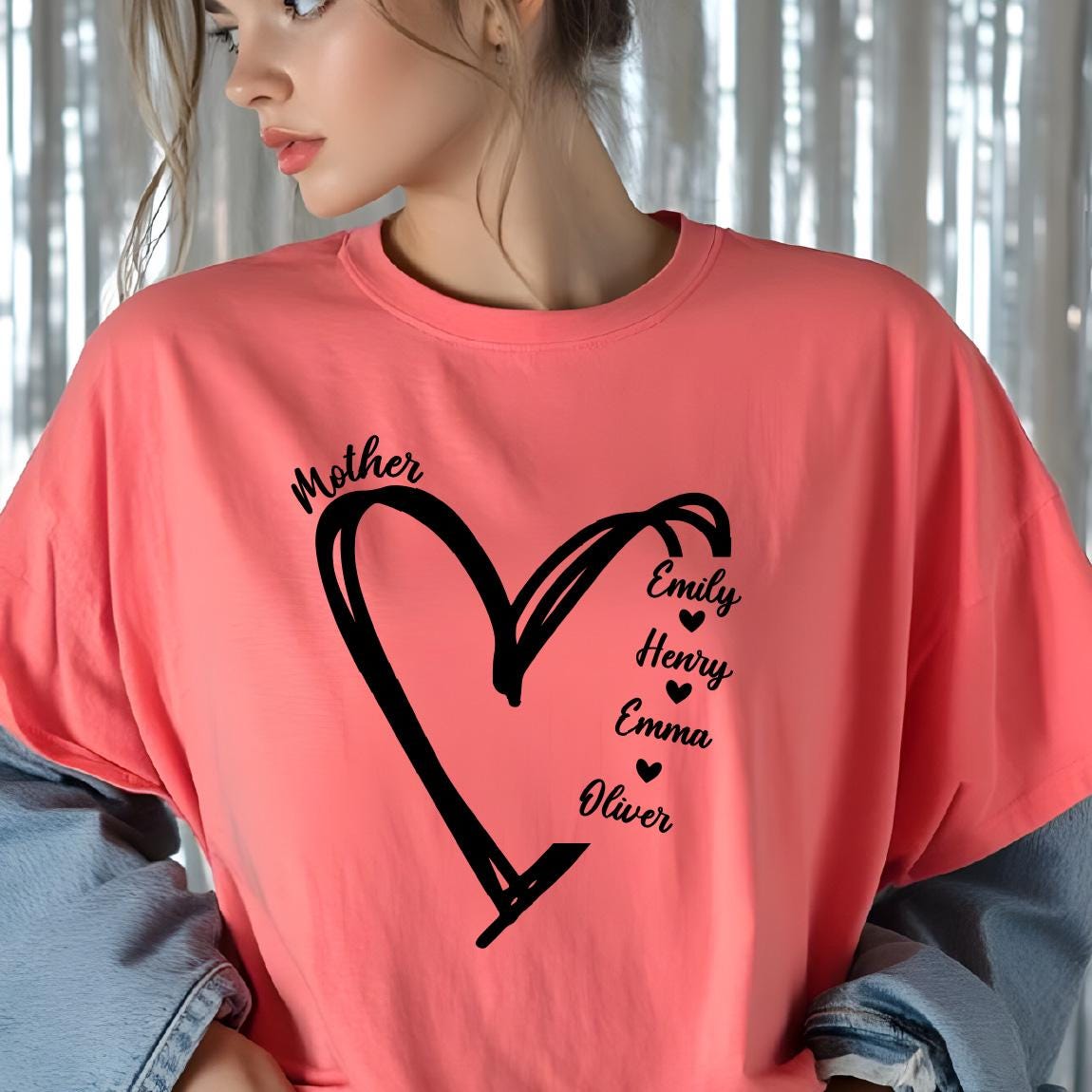 May include: A coral-colored short-sleeve t-shirt featuring a black graphic of a hand-drawn heart outline. The word Mother is printed above the heart, and the names Emily, Henry, Emma, and Oliver are listed vertically with small hearts in between.