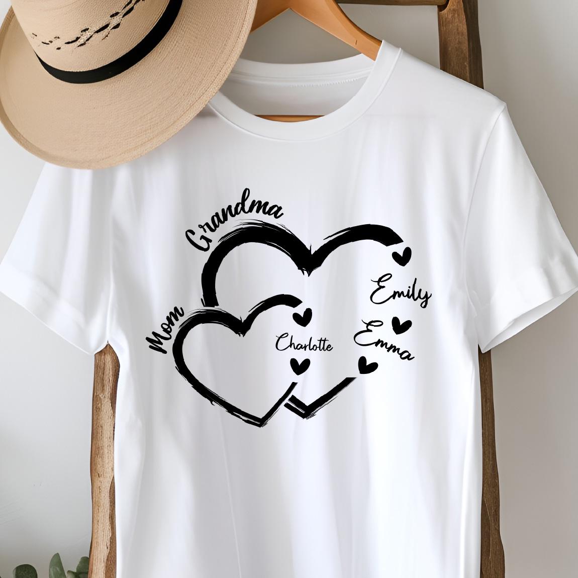 May include: White t-shirt with a black design of two interlocking hearts. The text "Grandma" is above the hearts, and the names "Mom", "Charlotte", "Emily", and "Emma" are inside the hearts.