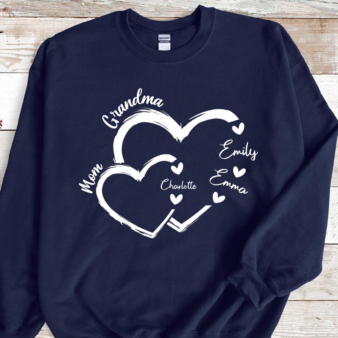 May include: Navy blue sweatshirt with a white design of two interlocking hearts. The text "Grandma" is above the hearts, and the text "Mom" is to the left of the hearts. Inside the hearts are the names "Charlotte", "Emily", and "Emma".