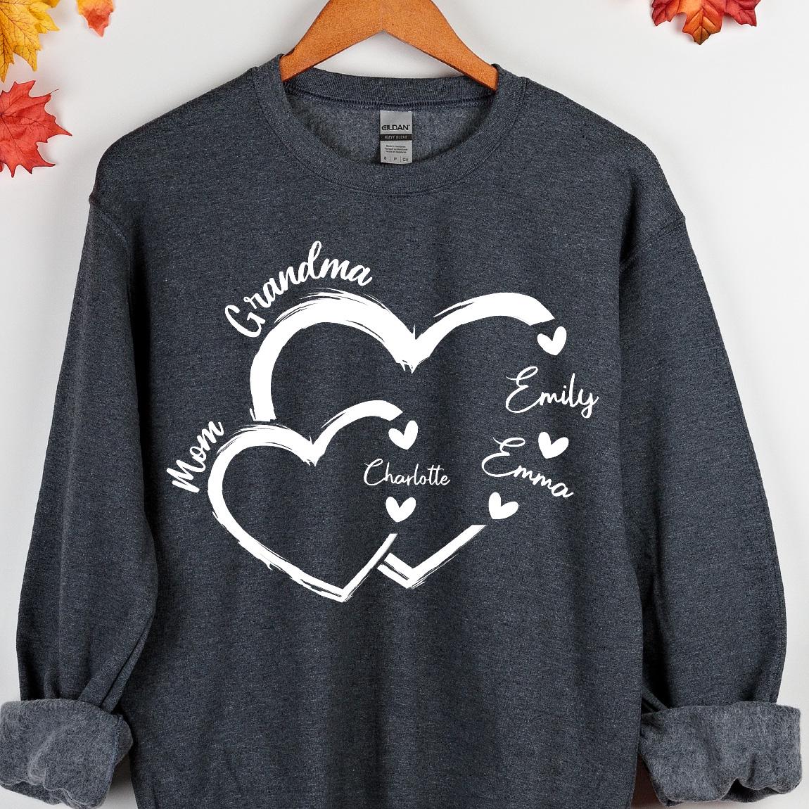 May include: A dark gray sweatshirt with a white design of two intertwined hearts. The text "Grandma" is above the hearts, and the names "Mom", "Emily", "Emma", and "Charlotte" are inside the hearts.