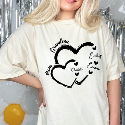 May include: Cream-colored t-shirt featuring a black heart design with the words "Grandma" and "Mom" incorporated. The names "Emily", "Emma", and "Charlotte" are also included. The shirt is a casual, everyday wear item.