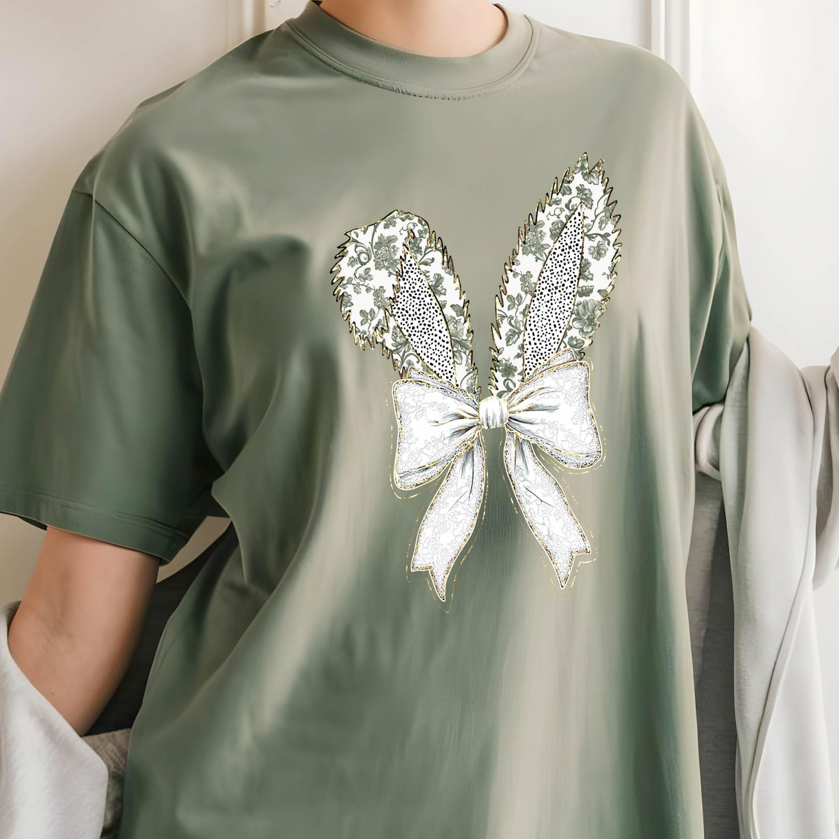 May include: A green t-shirt with a white and gold embroidered design of bunny ears and a bow.