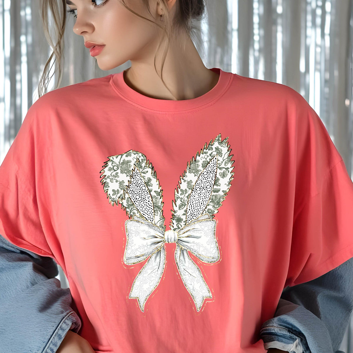 May include: A coral pink t-shirt with a white and gold embroidered design of bunny ears and a bow.