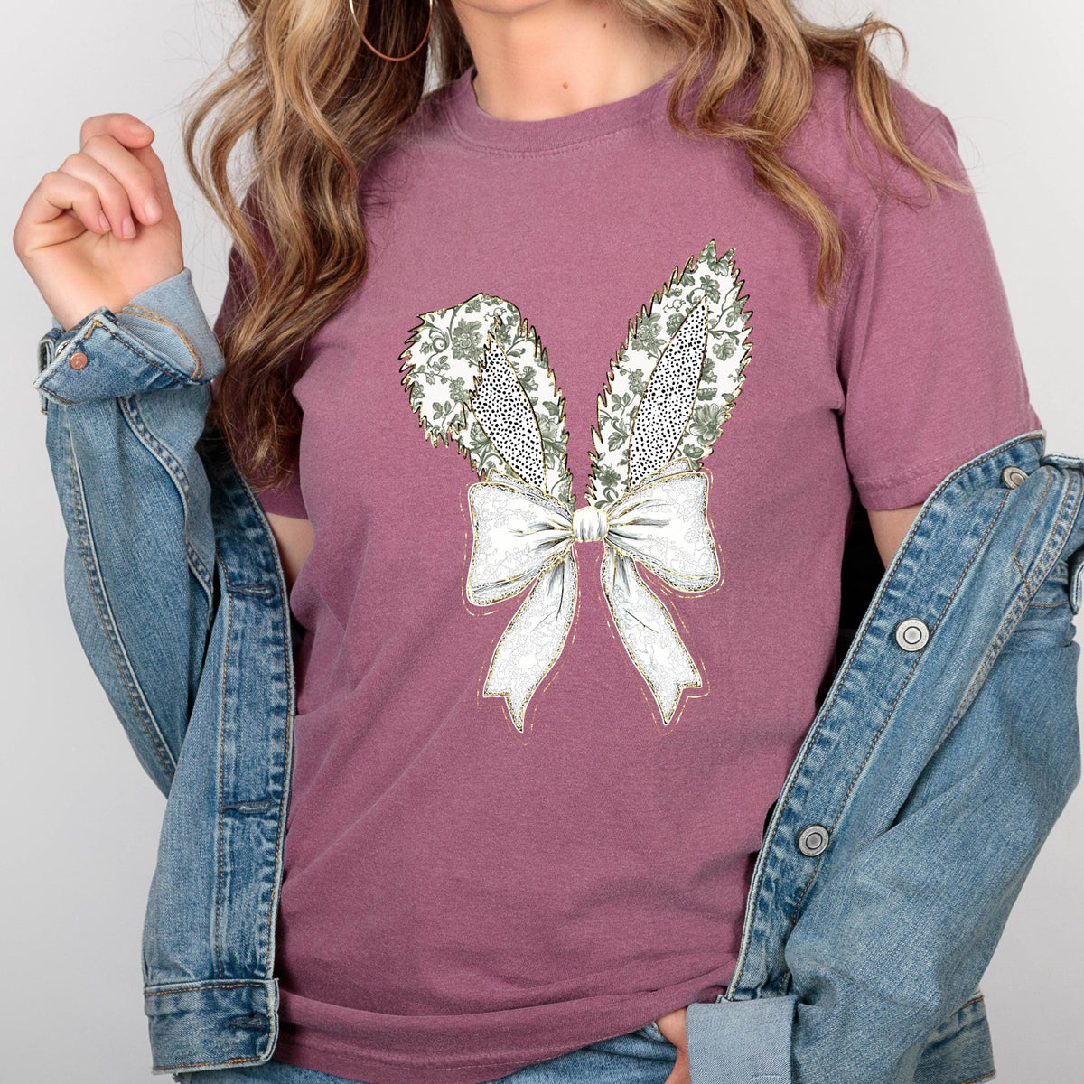 May include: A mauve t-shirt with a white and green floral design of bunny ears and a bow.