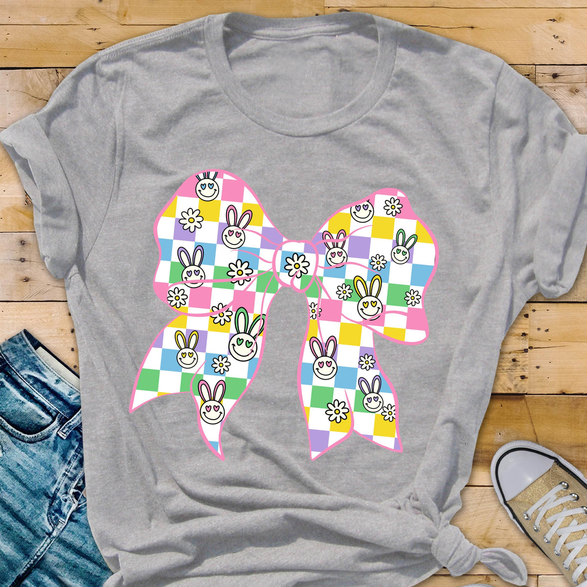 May include: A gray t-shirt with a pink bow featuring a checkered pattern with bunny faces and flowers. 