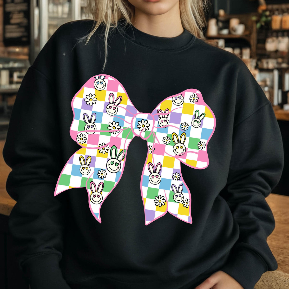 May include: Black sweatshirt with a large pink bow printed on the front. The bow is made up of a checkered pattern with bunny faces and flowers.