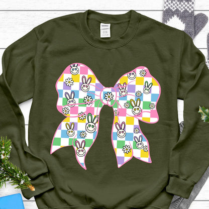 May include: A green sweatshirt with a pink and white checkered bow with smiling bunny faces. The bow has a green, yellow, and pink checkered pattern.