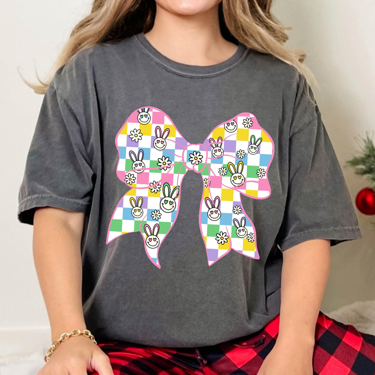 May include: A gray t-shirt with a pink bow printed on the front. The bow is checkered with a pattern of bunnies and flowers in shades of green, yellow, purple, and blue.