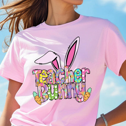 May include: A light pink t-shirt with the words "Teacher Bunny" in a colorful, patterned font. The design includes bunny ears and carrots, perfect for Easter or a teacher's gift.