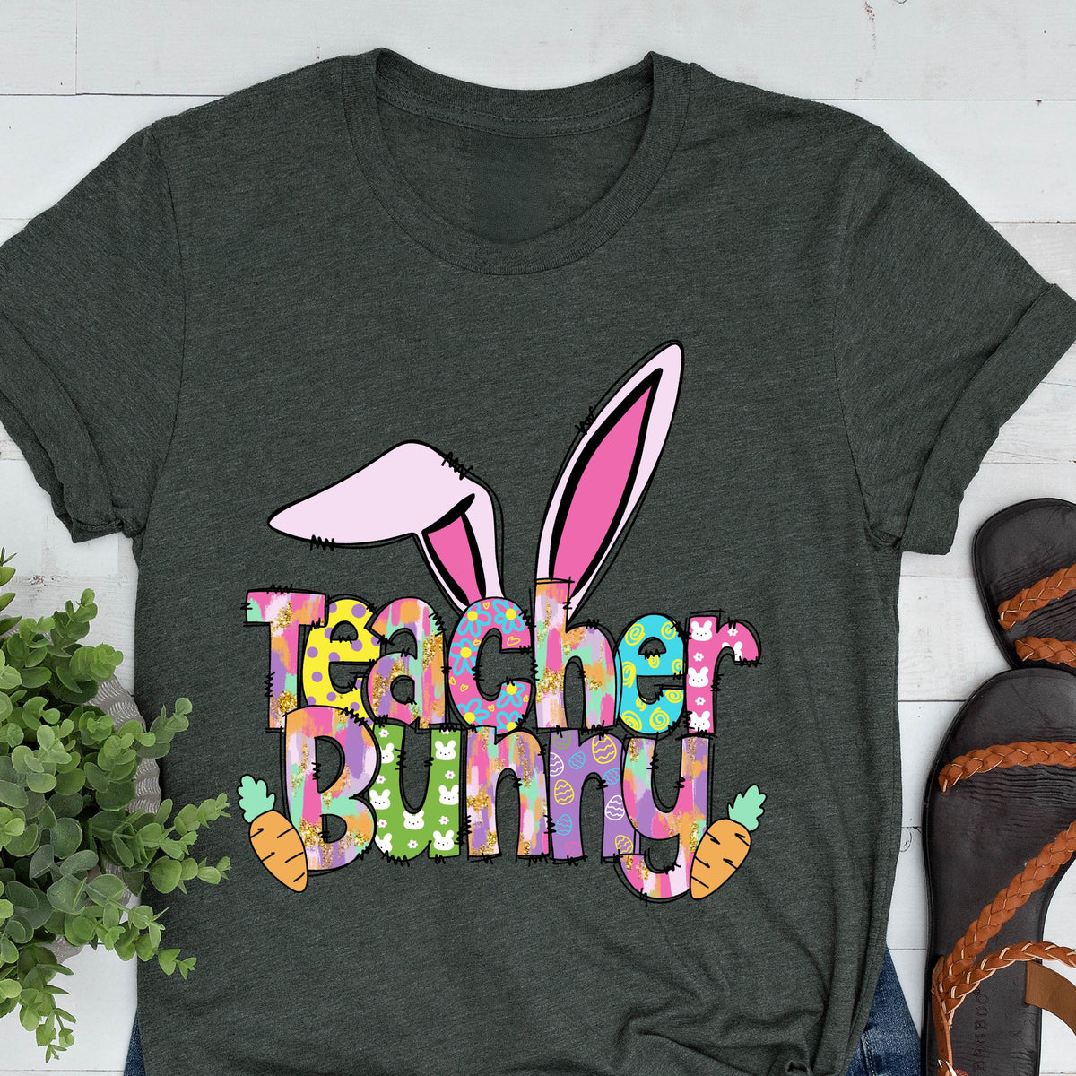 May include: Dark gray t-shirt with a colorful "Teacher Bunny" graphic. The design features bunny ears, carrots, and the words "Teacher Bunny" in a playful font. A fun and festive design for teachers.