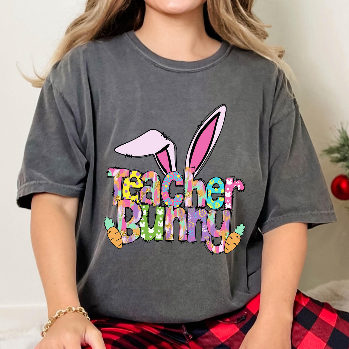 May include: Dark gray t-shirt with the words "Teacher Bunny" in colorful letters, bunny ears, and carrots. The shirt is a comfortable, casual style, perfect for Easter or a teacher's gift.