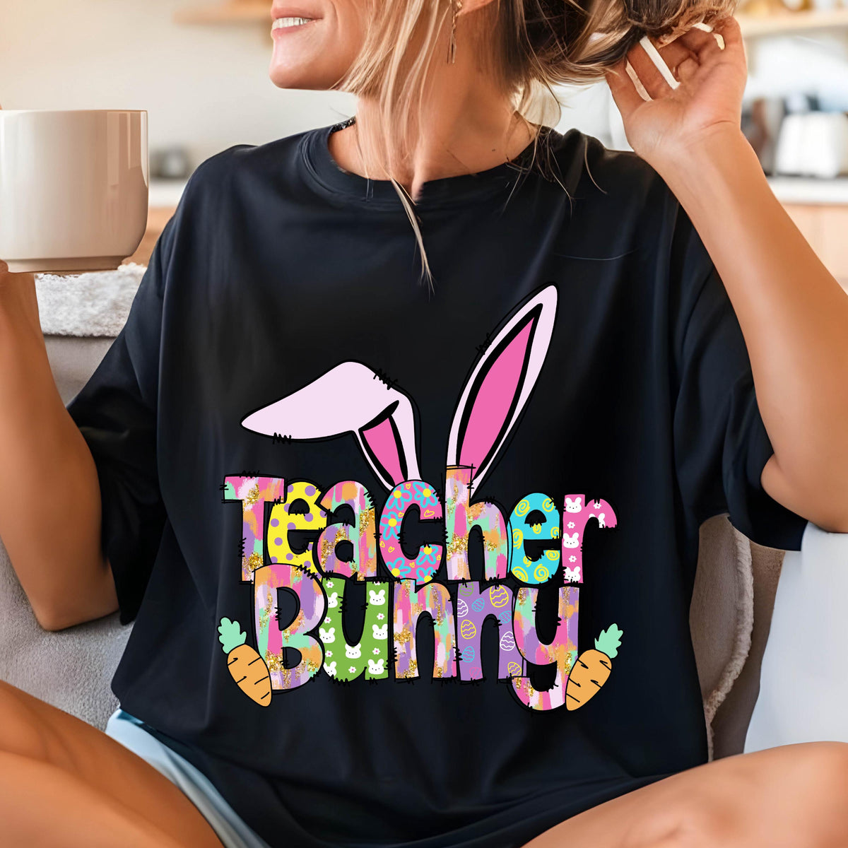 May include: Black t-shirt with a colorful "Teacher Bunny" graphic. The design features bunny ears, carrots, and the words "Teacher Bunny" in a playful font with Easter egg patterns. A fun, festive top for teachers.