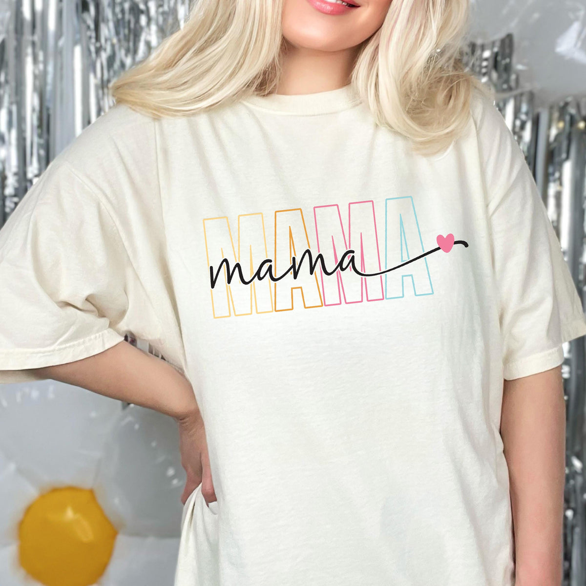 May include: A white t-shirt with the word "MAMA" in rainbow colors and the word "mama" in black script with a pink heart.