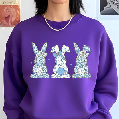 May include: Purple sweatshirt with a graphic of three blue and white bunny rabbits with bows. The bunnies are facing away from the viewer.