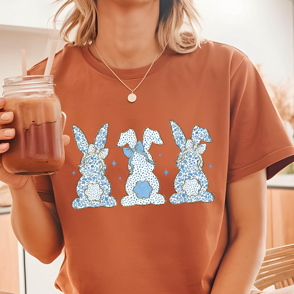 May include: A brown t-shirt with a graphic of three blue and white patterned bunnies with blue bows. The bunnies are facing away from the viewer.