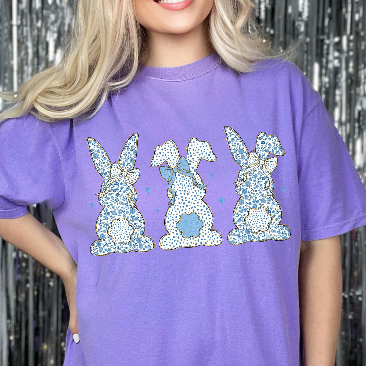 May include: Purple t-shirt with a graphic of three blue and white bunny rabbits with floral patterns and bows.
