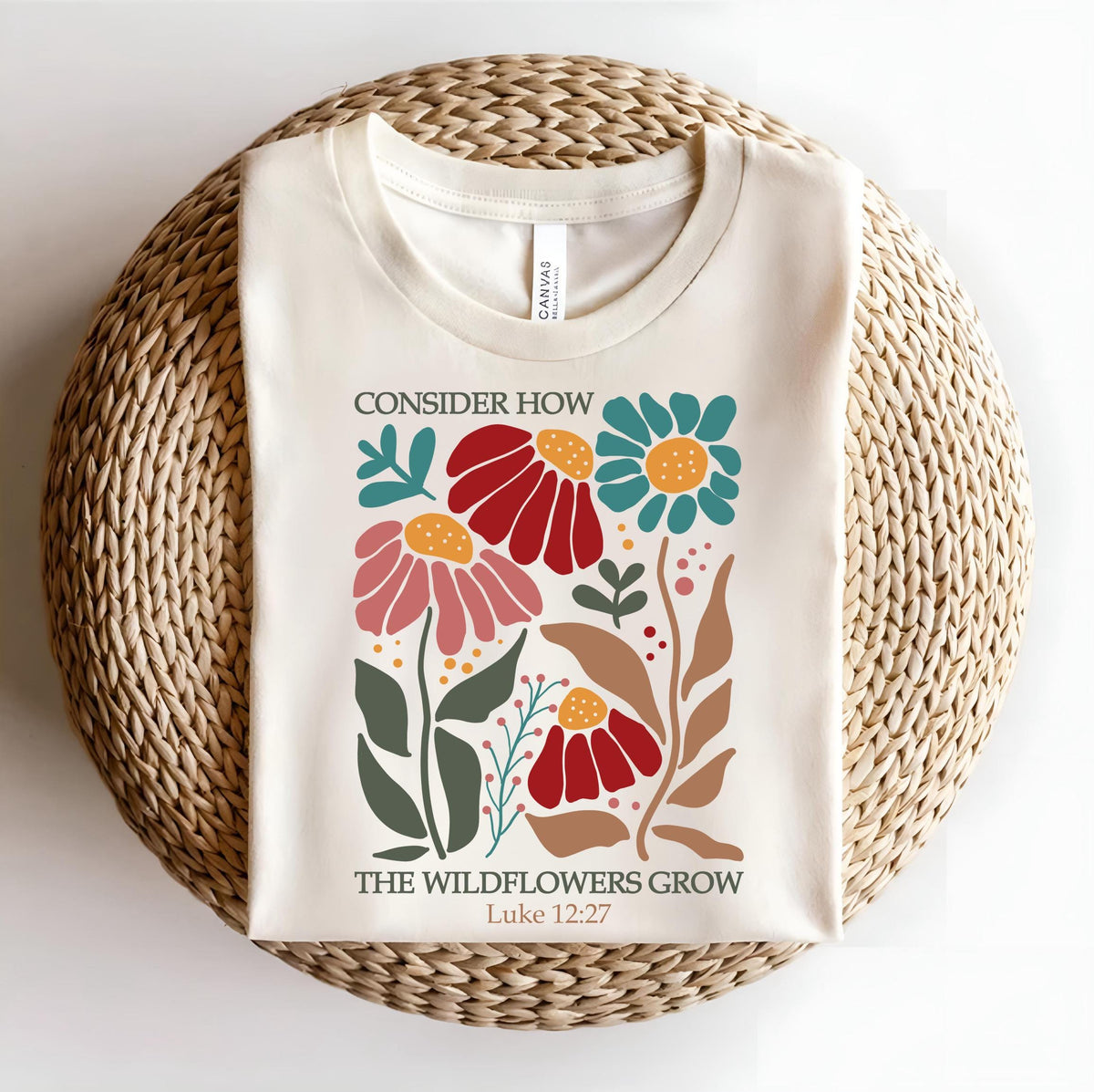 May include: A cream-colored t-shirt with a floral design and the text "Consider how the wildflowers grow Luke 12:27".