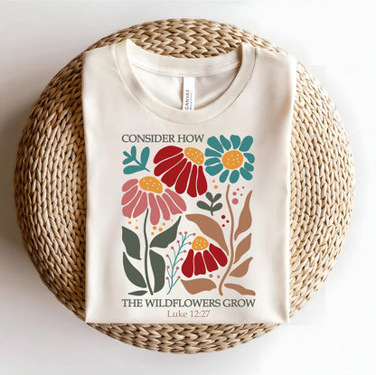May include: A cream-colored t-shirt with a floral design and the text "Consider how the wildflowers grow Luke 12:27".