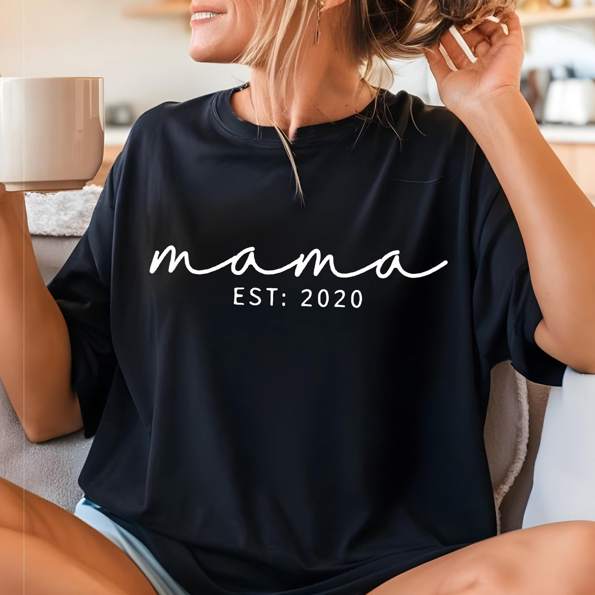 May include: A black short-sleeved t-shirt featuring the white text "mama" in a cursive script font, with the text "EST: 2020" printed in a clean, sans-serif font directly underneath the word "mama" on the center of the chest.