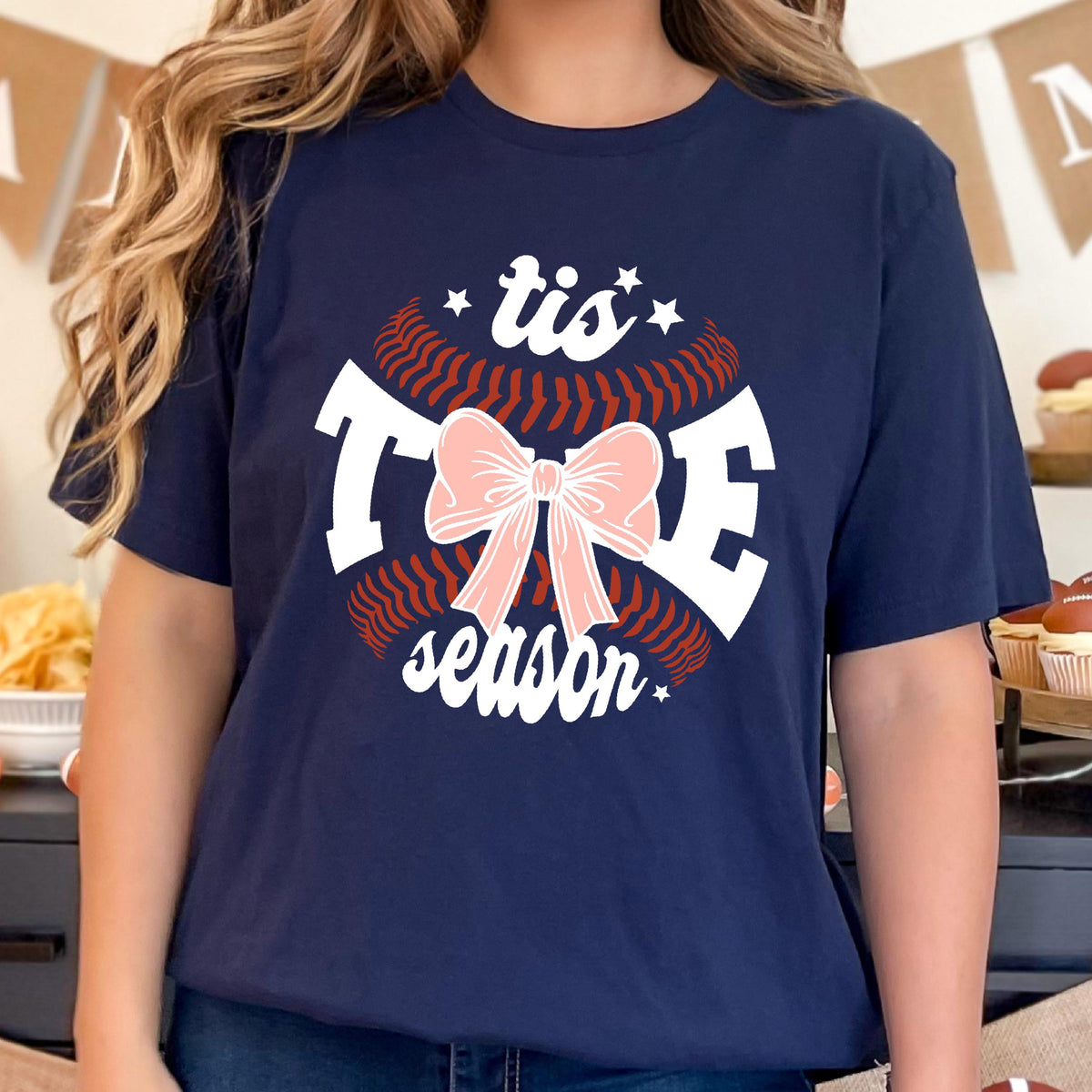 May include: Navy blue t-shirt with a white baseball graphic and the text "tis the season" with a pink bow in the center.