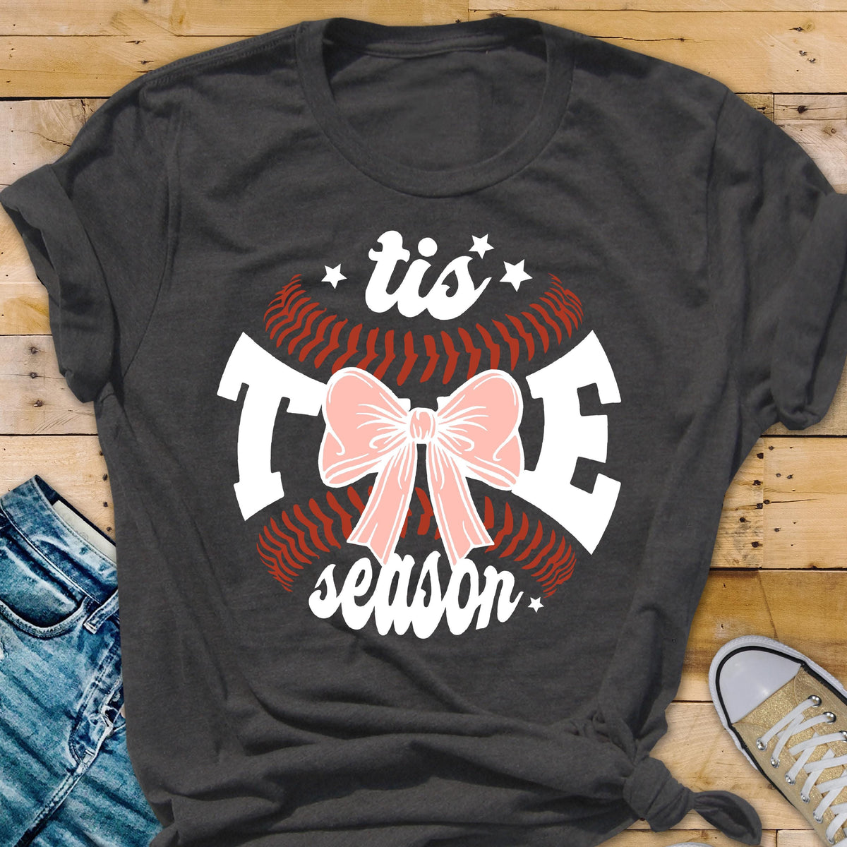 May include: A dark gray t-shirt with a white baseball graphic and the text "tis the season" with a pink bow in the center.